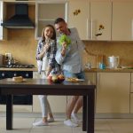 Attractive young joyful couple have fun dancing and singing while cooking in the kitchen at home in the morining