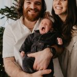 a man and woman holding a baby in front of a christmas tree